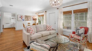 A spacious living room with a beige sofa, a glass coffee table, and a red armchair. There is a dining area with a white table and chairs in the background. - The "Water House" Cottages (Gulf Stream)