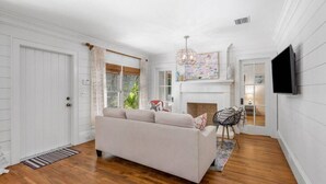 A spacious living room with a beige sofa, a fireplace, and a television mounted on the wall. - The "Water House" Cottages (Gulf Stream)