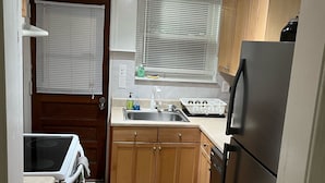 Une cuisine compacte avec des meubles en bois, un réfrigérateur en acier inoxydable, un évier et une fenêtre équipée de stores.