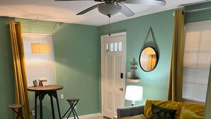 Un salon avec un canapé gris, une petite table, un ventilateur de plafond et une porte.