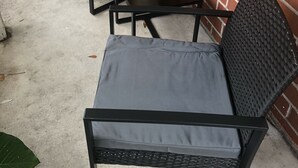 Un espace patio avec deux chaises en osier noir et une petite table, un mur en briques et une fenêtre avec des stores.