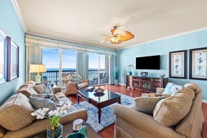 A spacious living room with a large window overlooking the ocean, a ceiling fan, and a flat-screen TV mounted on the wall. - $150 activities - E-gift card when you book - Stunning Oceanfront Retreat in Gated Community | M2303 (Myrtle Beach)
