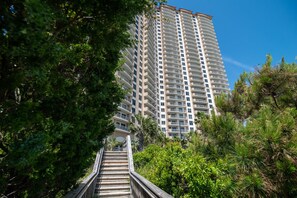 A tall residential building with multiple balconies, surrounded by lush greenery and a wooden staircase leading up to the entrance. - $150 activities - E-gift card when you book - Stunning Oceanfront Retreat in Gated Community | M2303 (Myrtle Beach)