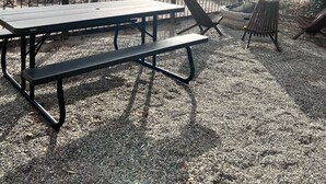 Ein Sitzbereich im Freien mit Picknicktischen und Stühlen, umgeben von Kiesböden und spärlicher Vegetation.