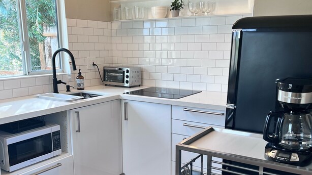Eine moderne Küche mit weißen Schränken, einem Einbauofen, einer Mikrowelle, einem Toaster, einer Kaffeemaschine und einem Fenster mit Blick auf Grünflächen.