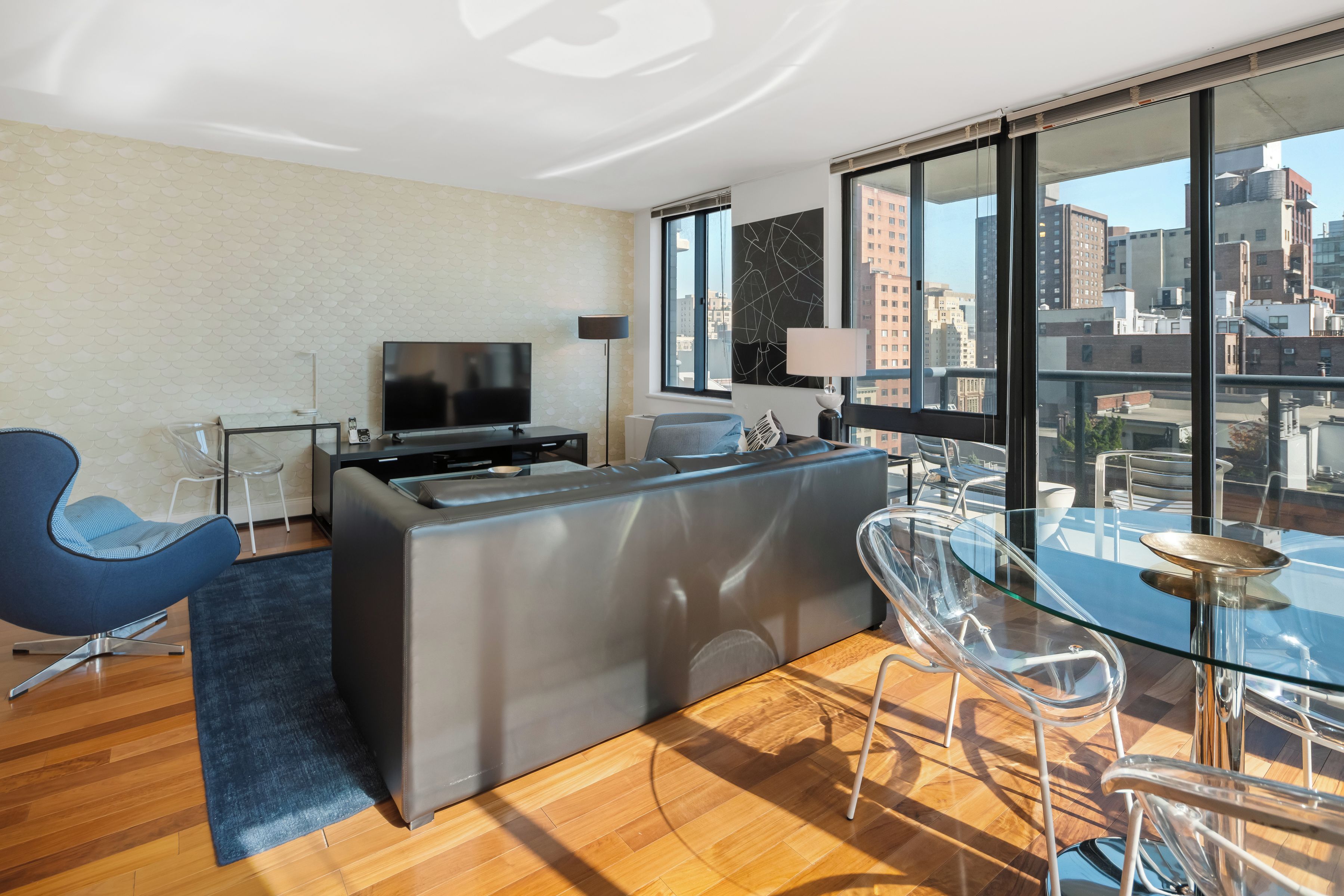 A modern living room with a glass dining table, a sofa, a TV, and a city view through large windows.