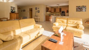 A spacious living room with a yellow sofa, a wooden coffee table, and a kitchen area in the background. - Lenerie - 800m plage - Wifi - Parking (Préfailles)