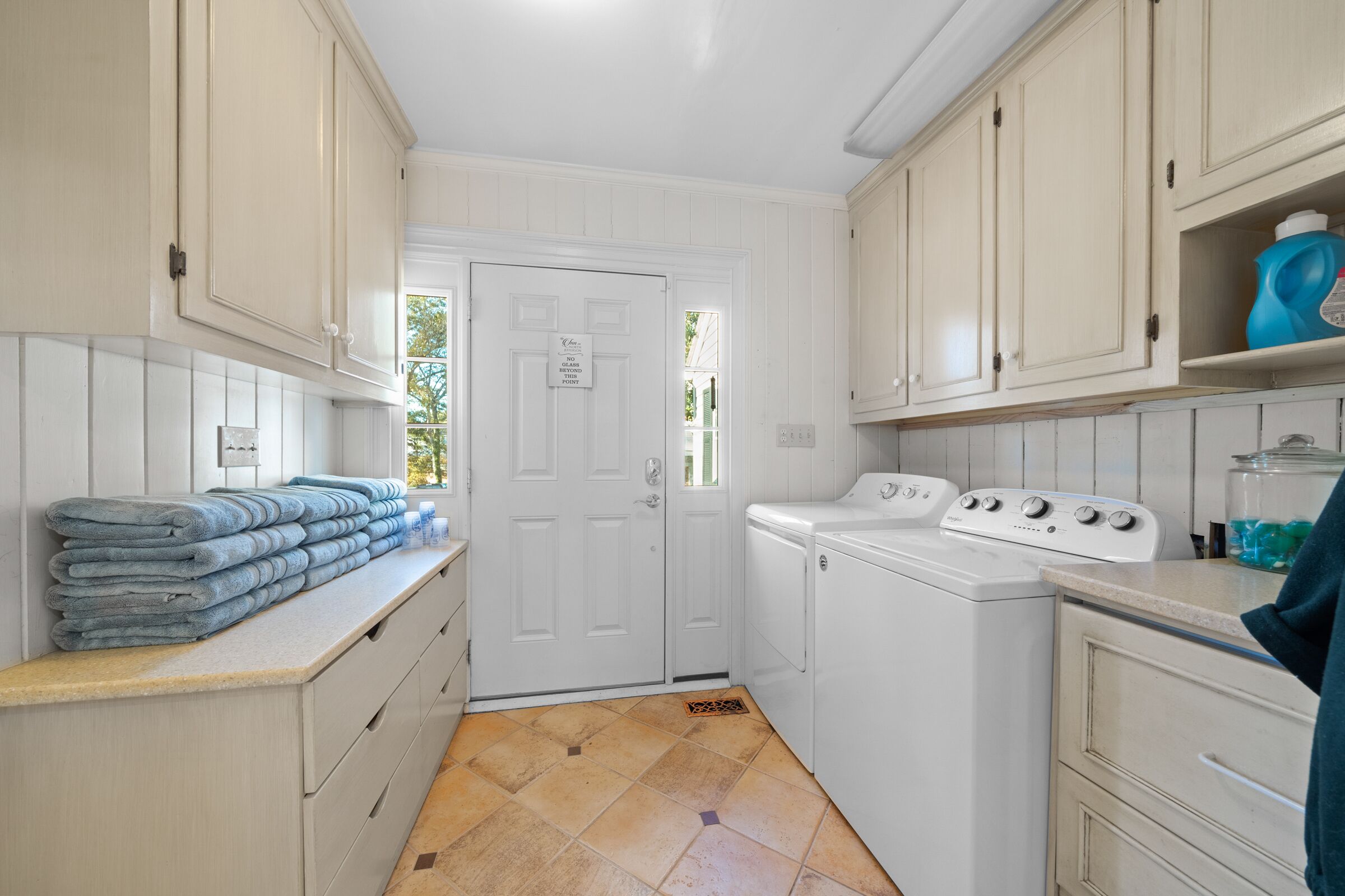A laundry room with a washing machine, stacked towels, and a door with a sign.
