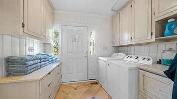 A laundry room with a washing machine, stacked towels, and a door with a sign.