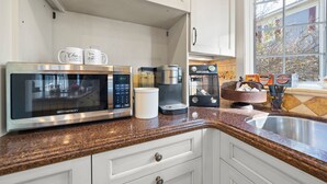 A kitchen with white cabinets, a granite countertop, a microwave, a coffee maker, and a window with a view of trees. - The Inn on North Jefferson (Milledgeville)