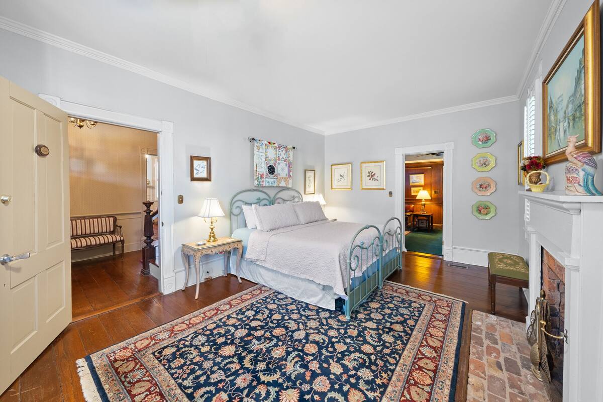 A bedroom with a bed, a nightstand, a lamp, a patterned rug, and a fireplace.