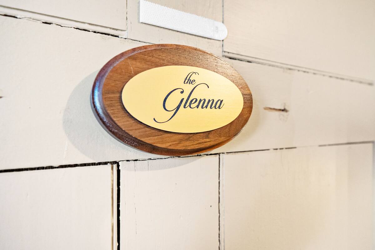 A wooden plaque with the text "the Glenna" mounted on a white wall.