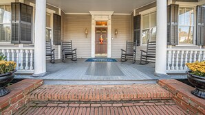 A porch with a wooden floor, two columns, and a door with a doormat. - The Inn on North Jefferson (Milledgeville)