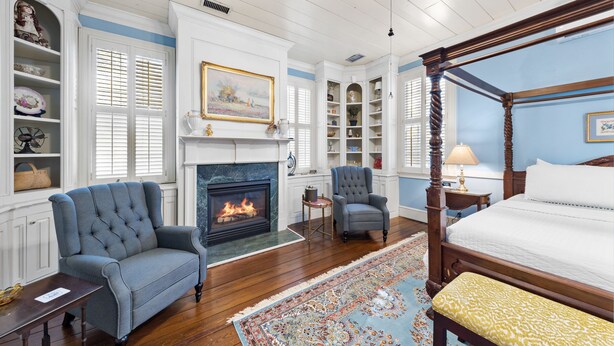 A bedroom with a four-poster bed, a fireplace, a blue and white color scheme, and wooden flooring. - The Inn on North Jefferson (Milledgeville)