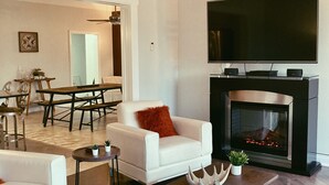 A modern living room with a fireplace, a flat-screen TV, and a dining area with a table and chairs.
