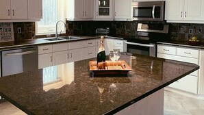 A modern kitchen with white cabinets, a large island with a bottle and glasses, and pendant lighting.