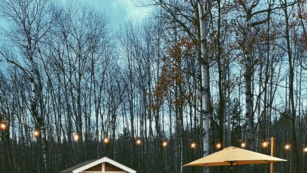 A hot tub surrounded by a wooden deck, a barbecue grill, and a small wooden cabin.
