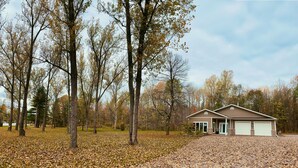 A two-story house with a garage, surrounded by trees and a leaf-covered ground.