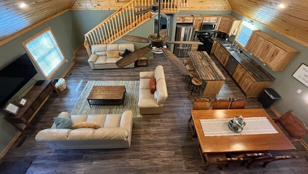 A spacious loft-style living area with a high ceiling, wooden beams, a built-in kitchen, and a cozy seating arrangement.