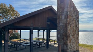 A covered picnic area with benches and a stone wall, overlooking a body of water.