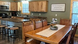 A spacious kitchen with wooden cabinets, a central island, and a dining area with a long wooden table and chairs.