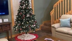 A cozy living room with a wooden ceiling, a Christmas tree, a sofa, a coffee table, and a staircase.