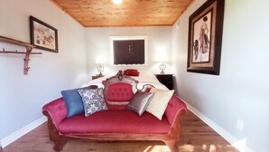 Un dormitorio con techo de madera, cama tapizada en rojo y dos mesitas de noche con lámparas.