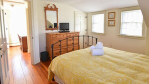 Une chambre à coucher comprenant un lit, une commode, un téléviseur et deux fenêtres.