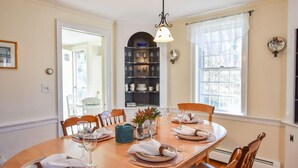 Een eetkamer met een houten tafel gedekt voor vier personen, een kroonluchter en een boekenkast met servies.