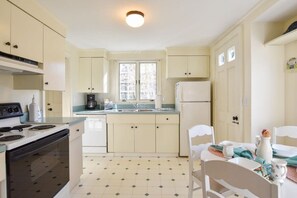 Een keuken met een fornuis, spoelbak en koelkast, en een eethoek met stoelen en een tafel.