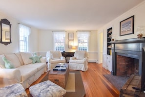 Een woonkamer met een open haard, een bank, twee fauteuils, een salontafel en een vloerkleed.