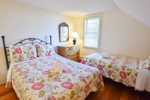 Une chambre avec deux lits, une table de chevet, un miroir et une fenêtre avec des stores.
