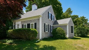 A two-story house with a gabled roof, a chimney, and a well-maintained lawn.