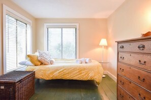 Une chambre à coucher avec un lit, une commode, une lampe et une fenêtre avec des stores.