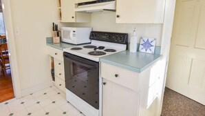 A compact kitchen with a stove, microwave, and oven. There are cabinets above the counter and a small window.
