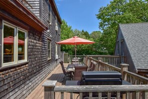 Un patio in legno con mobili da esterno, un barbecue e un ombrello rosso.