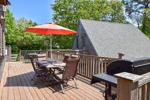 Un terrazzo in legno con tavolo e sedie, un barbecue e un ombrellone rosso.