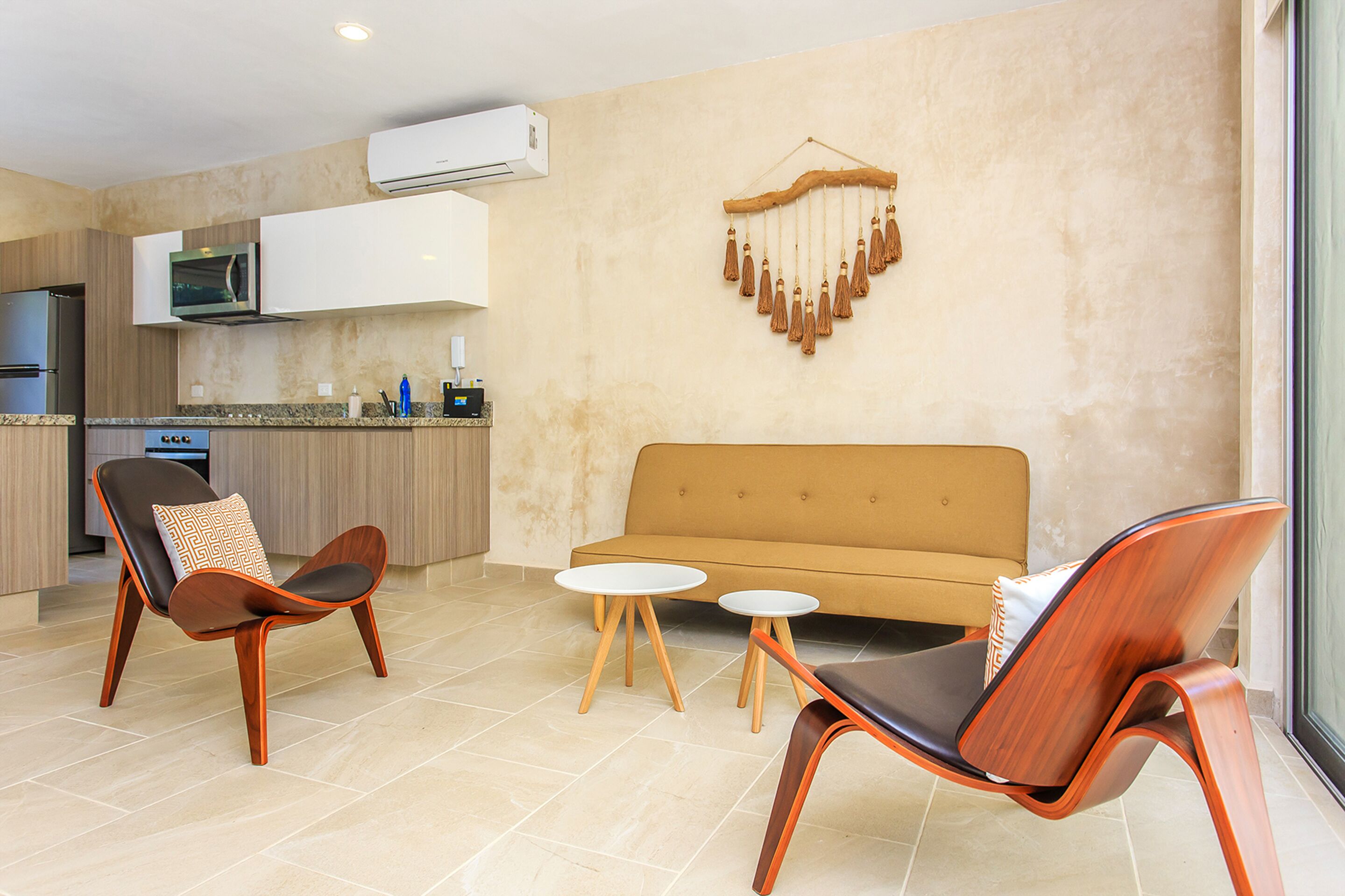 A modern kitchen with a microwave, stove, and cabinets. There is a sofa and two chairs with cushions. A decorative wall hanging is visible.