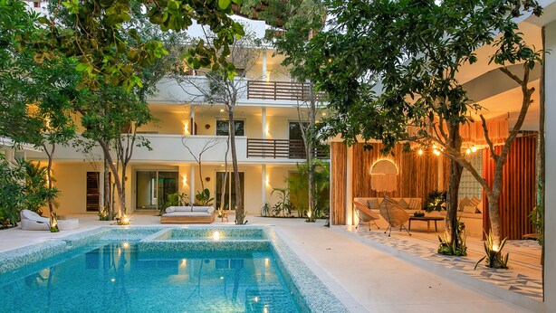 A pool area with a clear blue pool, surrounded by a white tiled deck, and a building with balconies and warm lighting. - Charming Nature-Inspired Condos with Sultry Surroundings by Stella Rentals (Tulum)