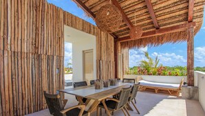 An outdoor patio with a wooden table and chairs, a woven ceiling, and a view of greenery. - Charming Nature-Inspired Condos with Sultry Surroundings by Stella Rentals (Tulum)