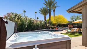 Ein Whirlpool in einem Garten mit Pool, Palmen und einer Terrassenanlage mit Liegestühlen.