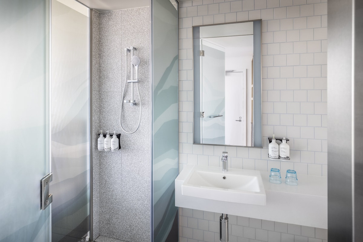 Une salle de bain moderne avec une douche à l’italienne en verre, un lavabo blanc et un miroir au-dessus.