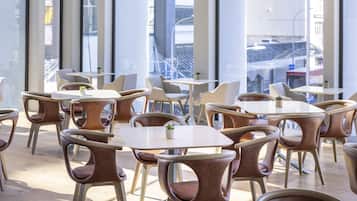 A modern interior with high ceilings, large windows, and a mix of round and square tables and chairs.