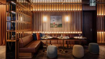 A modern interior with a wooden panel wall, a seating area with a sofa and tables, and a bookshelf with glass doors.