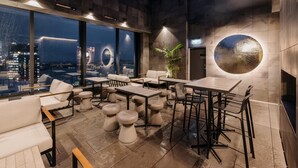 A modern indoor seating area with tables and chairs, large windows offering a city view, and a circular decorative element on the wall. - voco Auckland City Centre by IHG (Auckland)