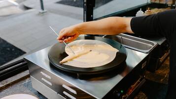 Une personne cuisine sur une plaque de cuisson et utilise une spatule pour manipuler une crêpe dans une poêle.