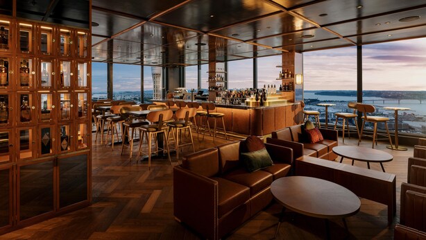 A modern bar area with a view of the city skyline, wooden furniture, and a variety of liquor bottles. - voco Auckland City Centre by IHG (Auckland)