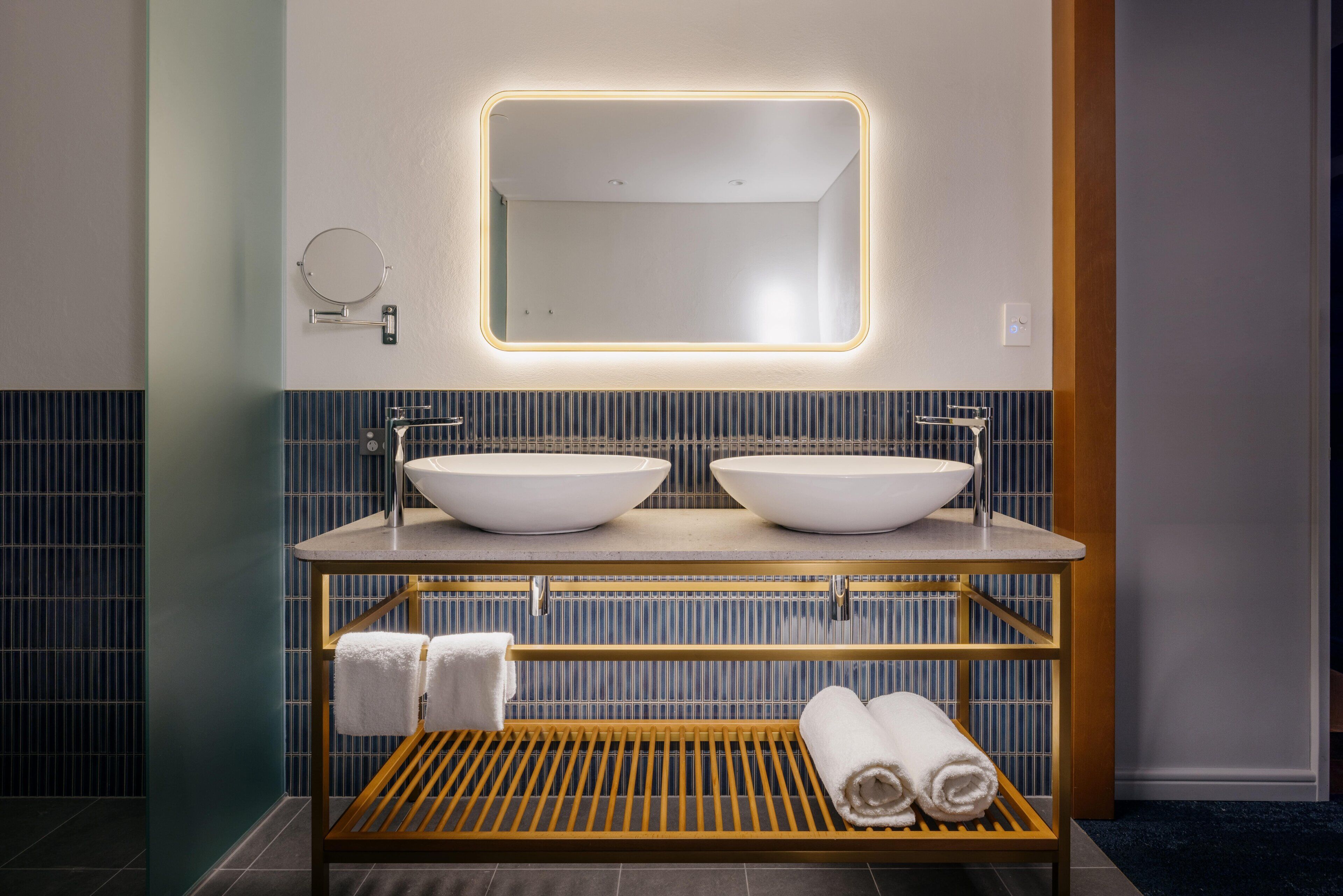 A modern bathroom with two sinks, a mirror, and a towel rack.