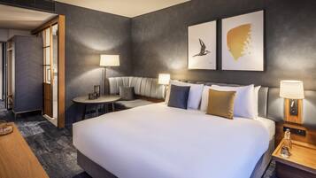 Una habitación de hotel moderna con una cama grande, zona de estar y obras de arte en las paredes.
