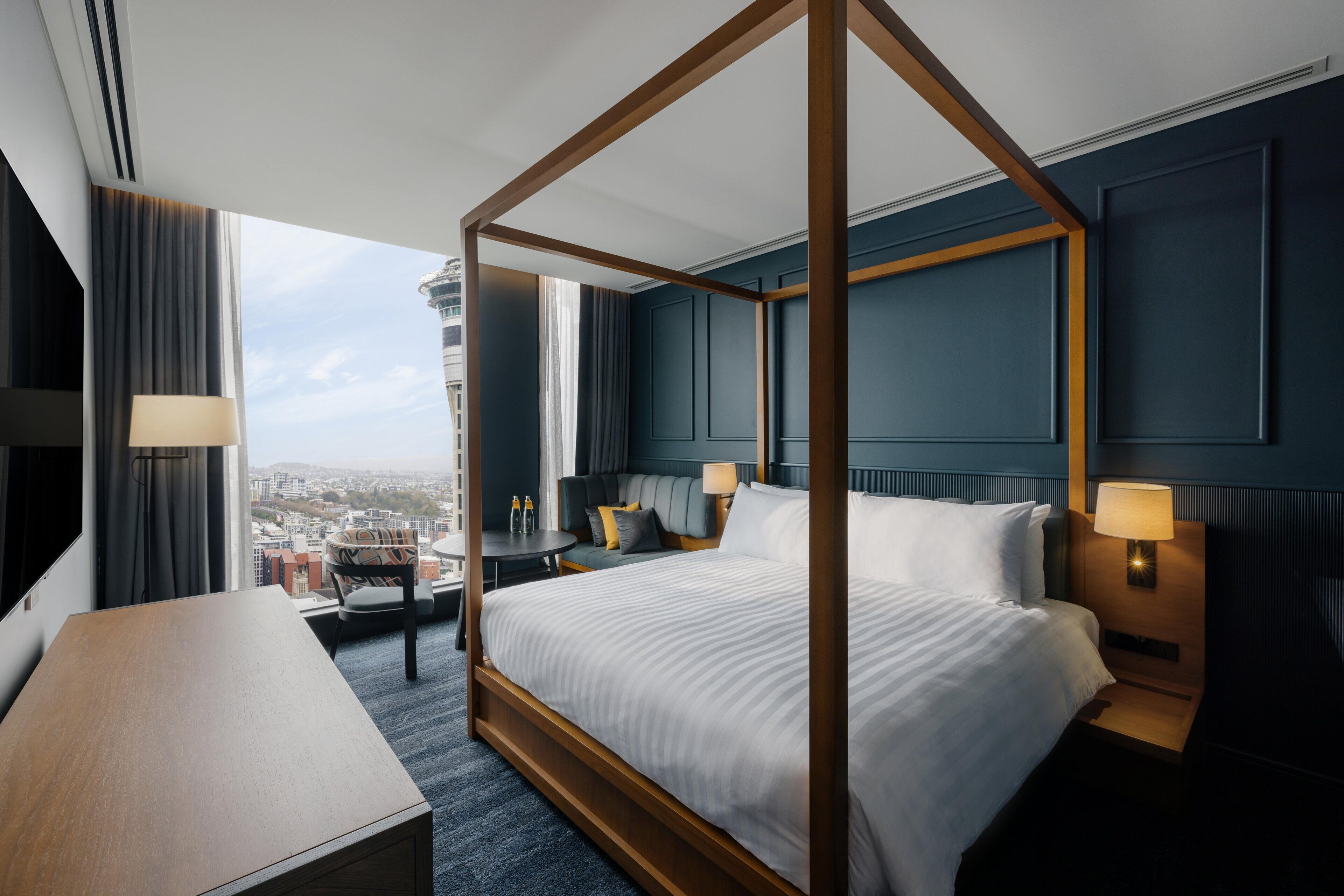 Un letto a baldacchino con vista sulla città, una scrivania e una sedia in una moderna camera d'albergo.